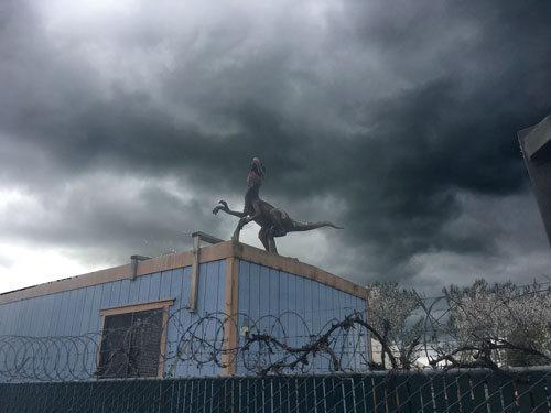 Velociraptor on roof above a wall with razor wire